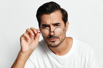 Thoughtful man adjusting glasses with a serious expression, wearing a casual white t-shirt,...
