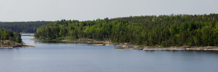 Bright yellow tent set up on rocky forested shore of calm northern lake, surrounded by dense trees...