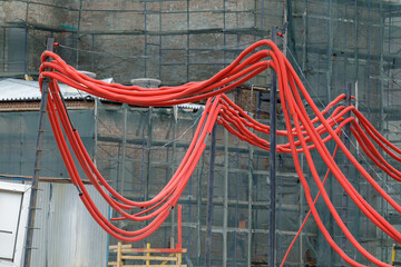 Bright red corrugated tubes suspended between poles at a construction site, likely used for...