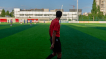 A referee in a red shirt watches players during a football match