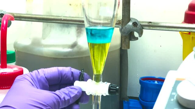 Separation of organic layer and water layer in separating funnel in a chemistry lab for education purpose. Effervescent of carbon dioxide bubble in organic layer. 4K scientific background concept.