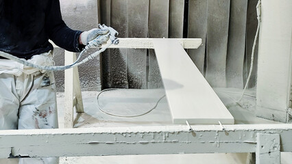Worker spraying white paint on wooden board in industrial workshop.