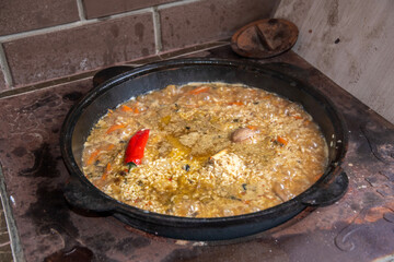 Traditional dish of pilaf is simmering in a cauldron on a wood burning stove, featuring rice,...