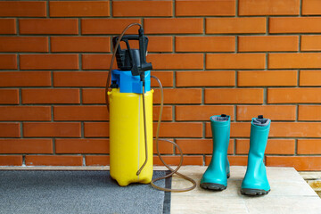Yellow garden sprayer and pair of turquoise boots are placed against red brick wall