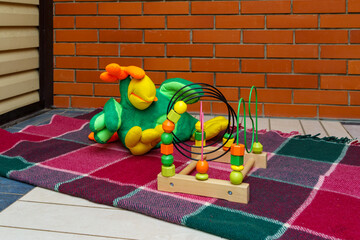 Colorful toy and wooden bead maze are placed on checkered blanket against brick wall