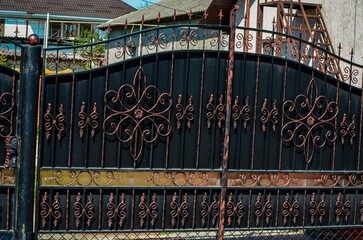 A black gate with gold and silver designs. The gate is on the side of a house. The gate is ornate...