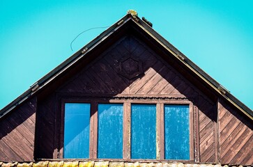 A house with a slanted roof and a window with three panes. The window is dirty and the roof is brown
