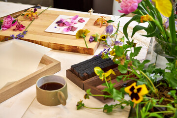 Botanical printmaking preparation – colorful fresh flowers arranged on board, DIY floral art setup in natural palette with hammer and craft tools, top view