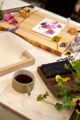 Creative flat lay of botanical printmaking with colorful flower petals, frame, coffee cup, and rubber stamps – cozy handmade workspace
