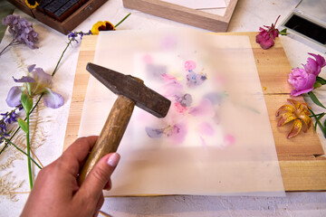 Botanical hammer art in action – flower pigments visible through parchment, wooden hammer resting...