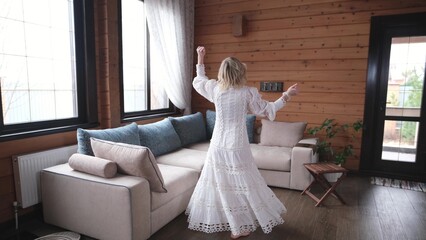 Happy young woman in traditional white dress spinning in big wooden house