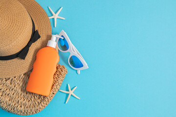 Summer vacation, UV protection concept. Orange sunscreen, sunglasses, straw bag, starfish, straw hat on blue background