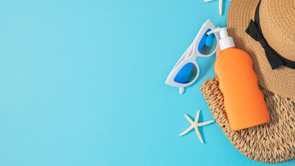 Safe tanning concept on the beach. Summer composition with sunscreen lotion, straw hat, bag, sunglasses and starfish on blue background. Banner.
