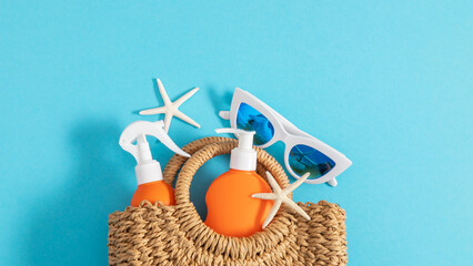 Safe tanning concept on the beach. Sunscreen lotion, cream, straw bag, starfish, sunglasses on blue background, close-up. Summer vacation concep