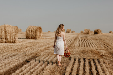 Beautiful young blonde girl in a field with haystacks in summer