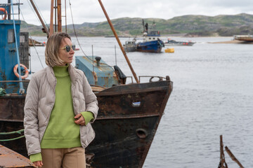 Woman standing near rusty abandoned fishing boats at the ship graveyard in Teriberka