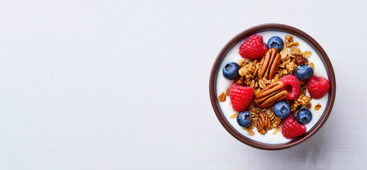 Fototapeta premium Healthy breakfast bowl with yogurt granola pecans raspberries blueberries on white background top view high protein clean eating diet nutrition, copy space 
