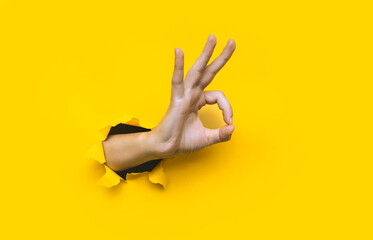 A right woman's hand shows with a gesture that everything is fine (ok). Torn hole in yellow paper....
