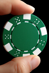 Green poker chip held by a person against a dark background in a gambling setting