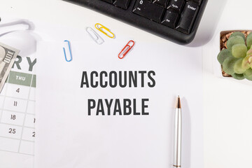 A handwritten note reading "Accounts Payable" rests on a wooden desk beside bundles of cash, symbolizing financial obligations and short-term liabilities in business accounting.

