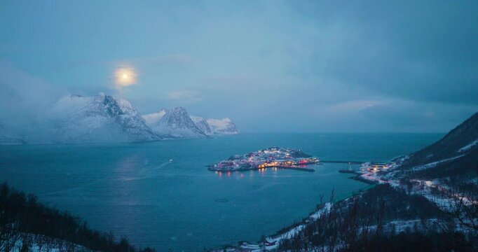 Hus&oslash;y bei Senja in Nordnorwegen am Morgen im Schneesturm, durch die verwehte Schneeluft scheint der Vollmond &uuml;ber der winterlichen K&uuml;stenlandschaft in der Fjordregion von Troms og Finnmark 
