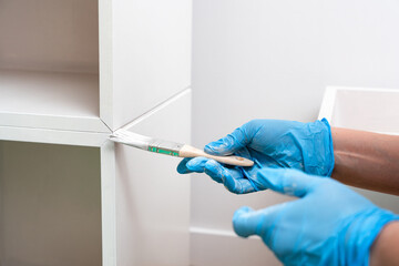 Person Painting Wooden Shelf Joint with Brush in Blue Gloves