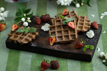 Vienna waffles decorated with strawberries and jasmine flowers on a green background
