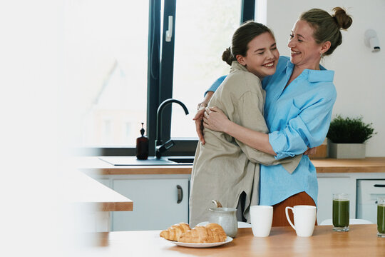 Middle-aged woman embracing younger woman in a bright kitchen showing active healthy lifestyle and wellbeing together