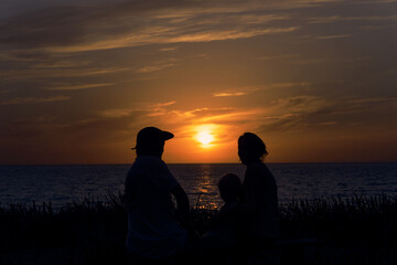 Family silhouetted against a breathtaking sunset over the Alpine mountains reflecting on a serene...