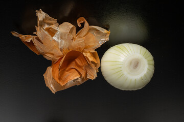 Peeled onion and onion peel next to it on black table and vegetable peeling knife.Close up of dry...