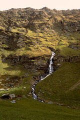 Serene alpine landscape with a flowing waterfall amidst rocky mountains and lush green valleys...
