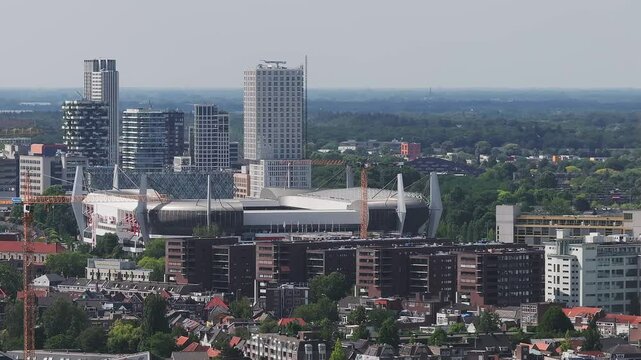Aerial view of Eindhoven, Netherlands, with Philips Stadion, modern buildings, greenery, and construction cranes in a slow sweeping pan.