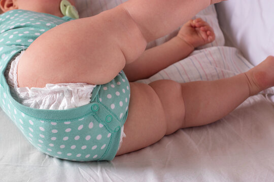 An eight-month-old baby turns over from his back to his stomach, lying on bed. Legs of newborn baby in the crib