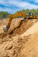 Obraz premium A caterpillar tractor works with a bucket in a sand pit. Sand mining