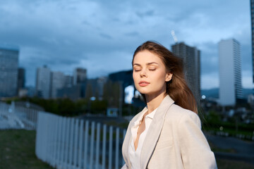 Woman in beige business suit with closed eyes in urban outdoor setting expressing calm and...