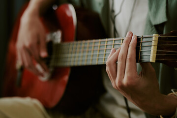 Teenage Caucasian boy playing acoustic guitar at home, close up of hands strumming and pressing...