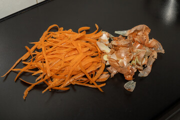 Onion peel and carrot waste on black table and vegetable peeling knife.View of pile of various...