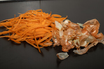 Onion peel and carrot waste on black table and vegetable peeling knife.View of pile of various...