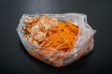 Onion peel and carrot waste in bio bag on black table and vegetable peeler.View of pile of various...