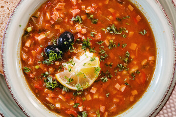 Homemade solyanka soup with lemon and herbs in a plate.