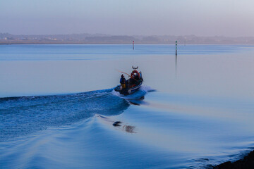 A small boat with fishermen cuts through calm blue waters under a partly cloudy sky