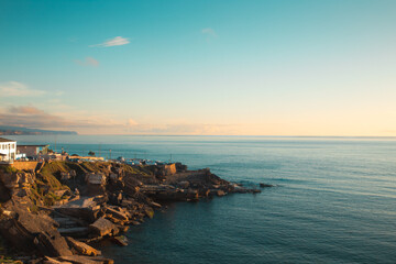 Golden hour sunlight bathes the rocky coastline of Ericeira, Portugal, as the calm Atlantic Ocean stretches out to the horizon under a tranquil sky