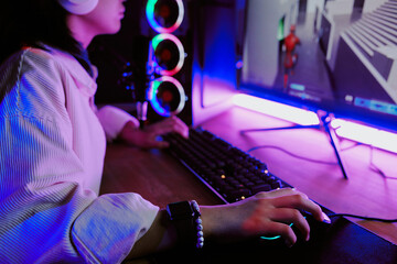 Teenage girl live streaming video games at home, wearing headphones and using gaming computer with RGB lighting, hand on mouse, focused on screen, engaging in online gameplay