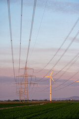 Renewable and traditional energy sources meet: power lines and a wind turbine stretch across...