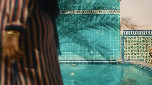 Serene pool at moroccan riad hotel evokes vacation bliss with mosaic walls and turquoise water for summer relaxation.