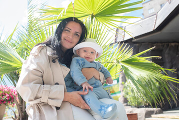 woman with 6 month old baby sitting near palm tree in summer