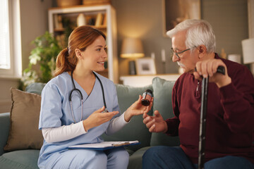 In a home setting, a kind female Home health nurse provides medication instructions to an elderly...