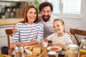 A family gathers around the kitchen table for a joyful breakfast. They share laughter, enjoy tasty food, and capture a moment of happiness together.
