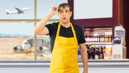 Hispanic barista wearing employee apron.Surprised pointing with finger to the side, open mouth amazed expression in the coffee shop at an airport