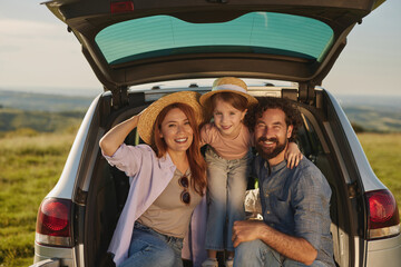 A family is gathered at an outdoor picnic, smiling joyfully near their car in a beautiful natural...
